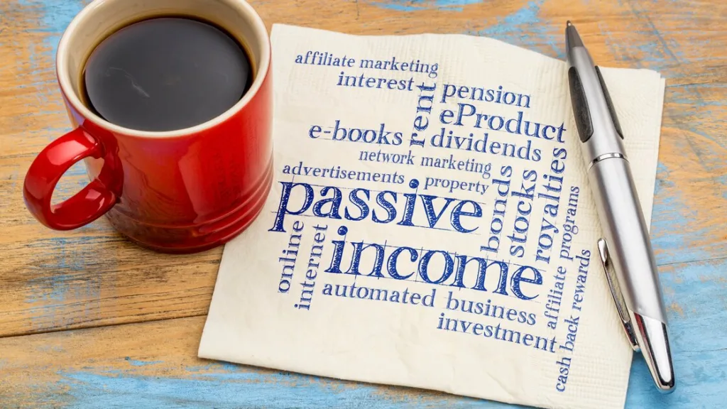 A red mug with coffee sitted on a wooden table top, next to the cup is a piece of paper written the words 'Passive Income' in high font size to show it is the main text. Passive income strategies like affiliate marketing, ebooks, etc are written in reduced font all around the main text.